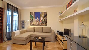 A living room with a sectional sofa, a coffee table, a TV, and a bookshelf.
