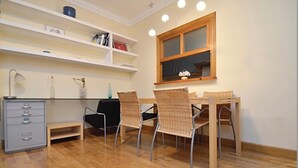 A dining area with a wooden table and four wicker chairs, a white cabinet with drawers, and a window with a wooden frame.