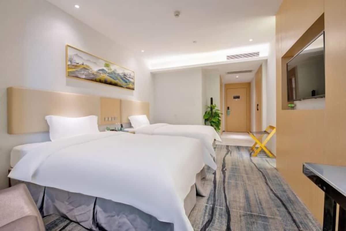 A hotel room with two beds, a painting on the wall, a plant, and a TV on the right side.
