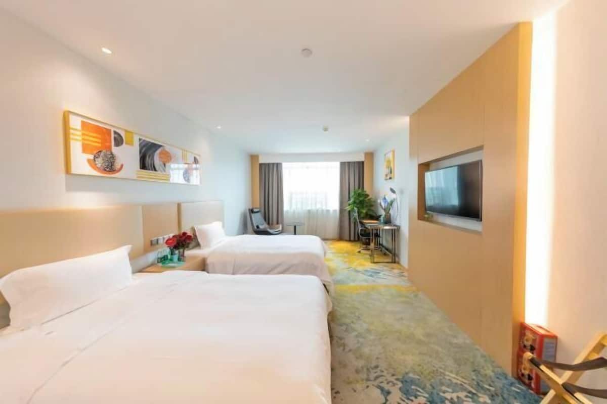 A hotel room with two beds, a TV, a desk with a chair, and a window with curtains.