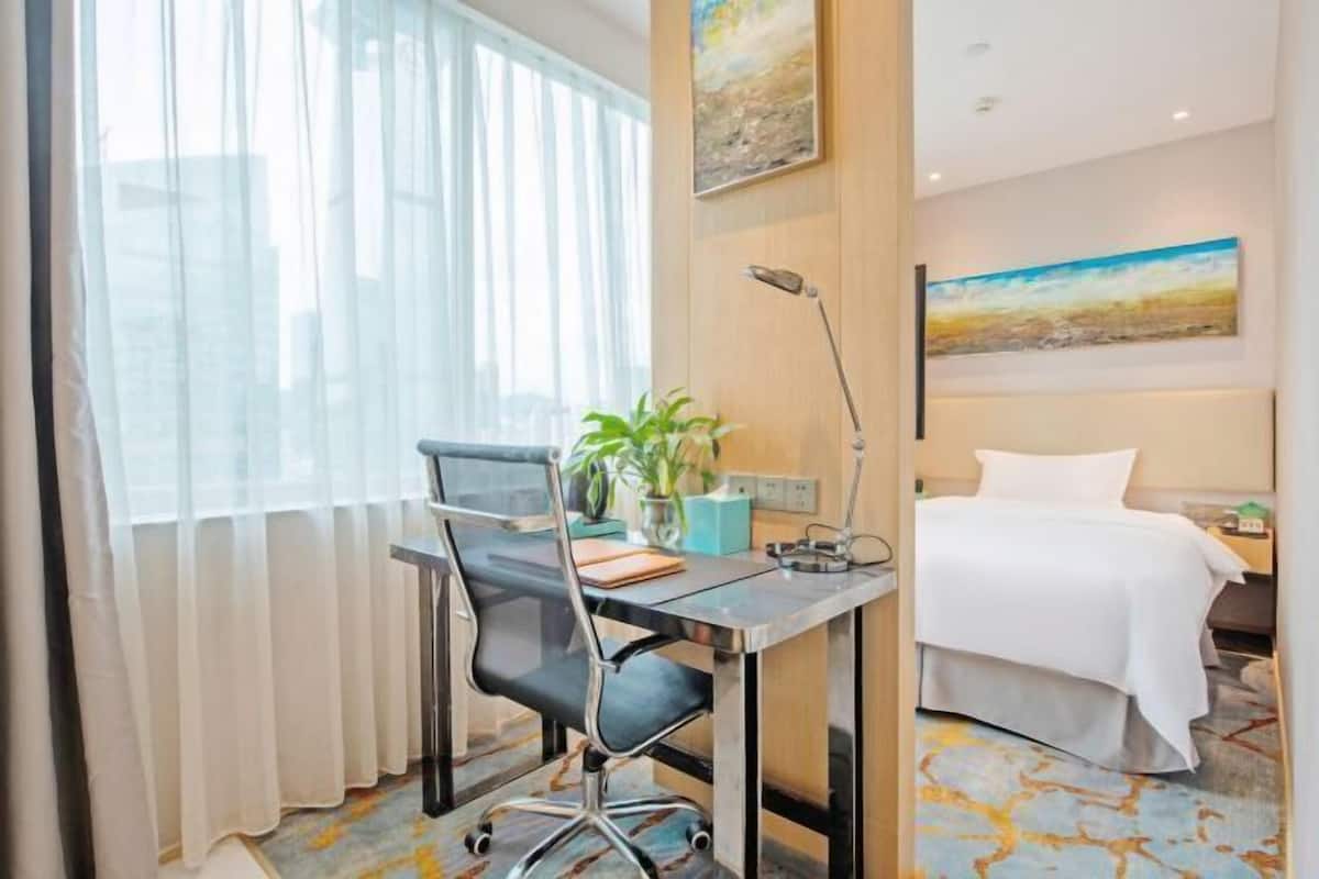 A hotel room with a desk, chair, bed, and a painting on the wall.