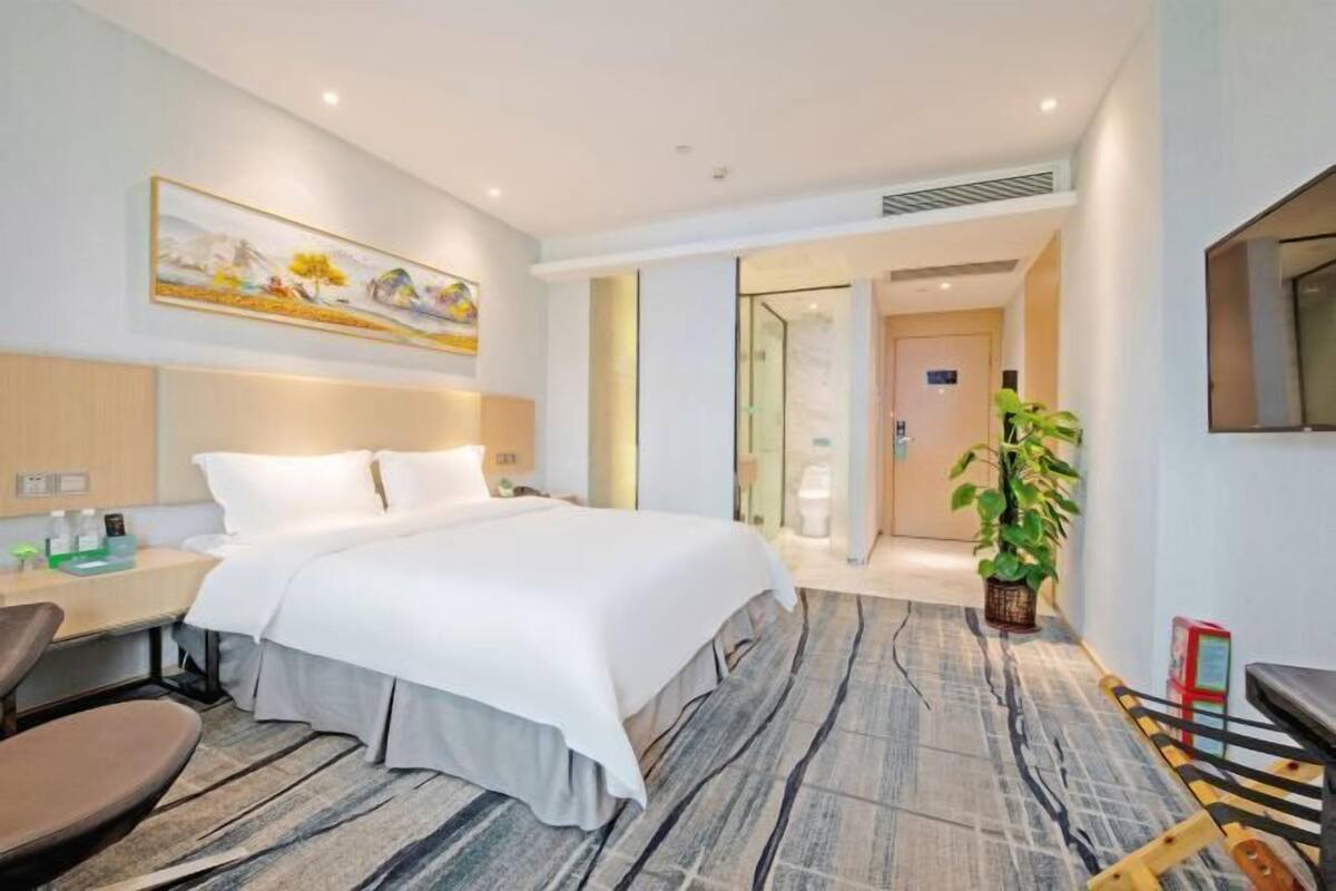 A hotel room with a bed, bedside table, chair, and a painting on the wall.