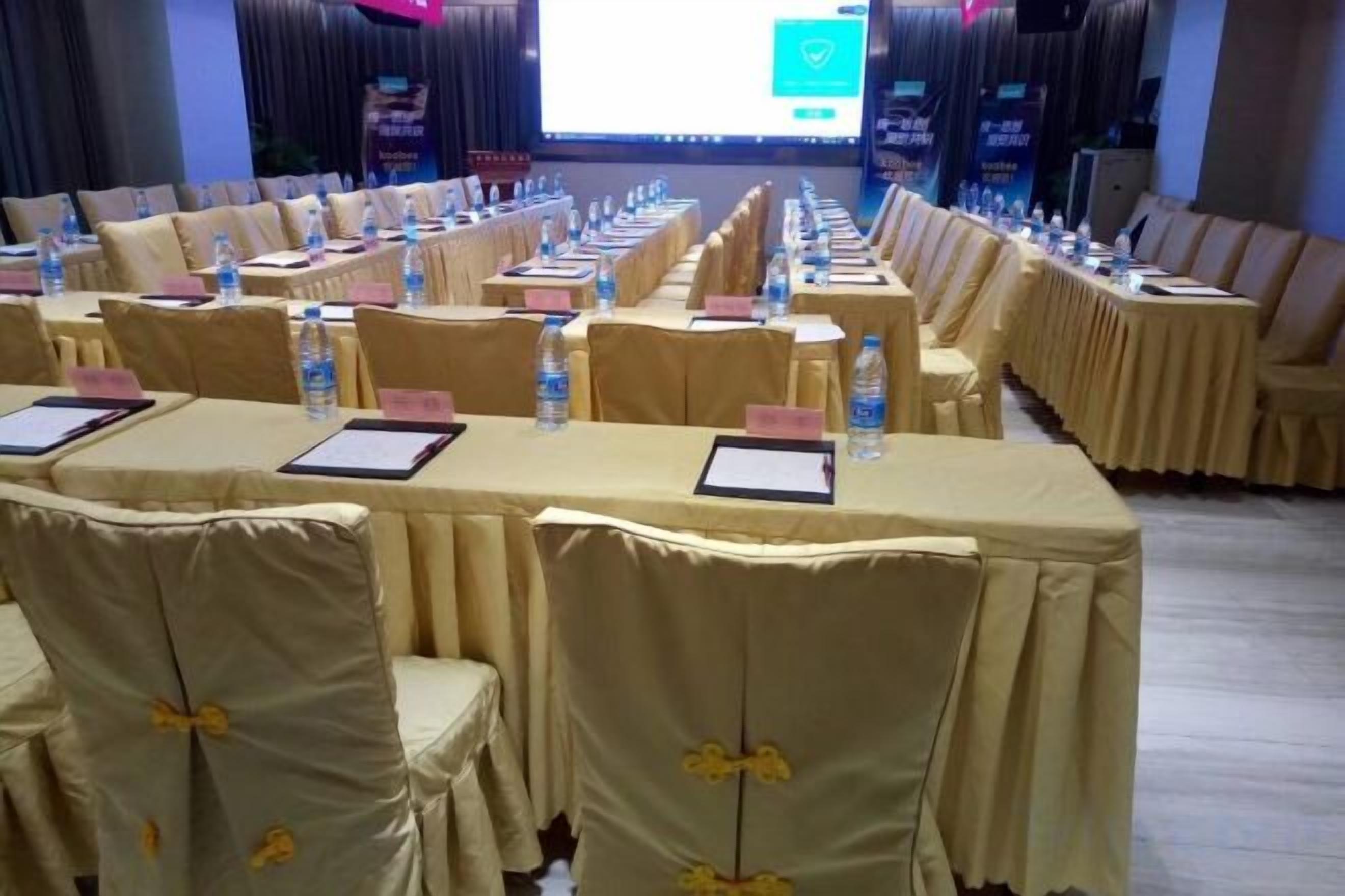 Un salón de conferencias con filas de mesas, sillas y placas de identificación, equipado con botellas de agua y blocs de notas.