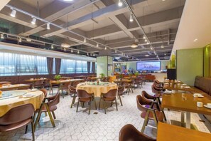 A spacious dining area with round tables and chairs, large windows, and a television screen. - Wanguo International Hotel (Shenzhen)