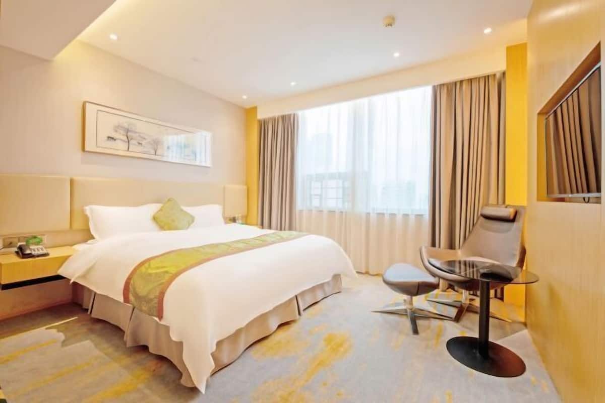 A hotel room with a large bed, a desk, a chair, and a window with curtains.