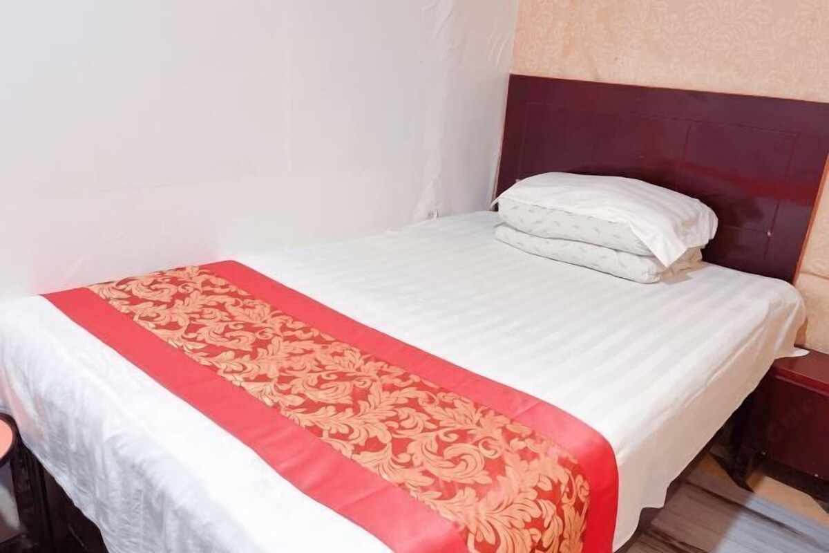 A neatly made bed with a white and red bedspread, a wooden headboard, and a wooden nightstand beside it.