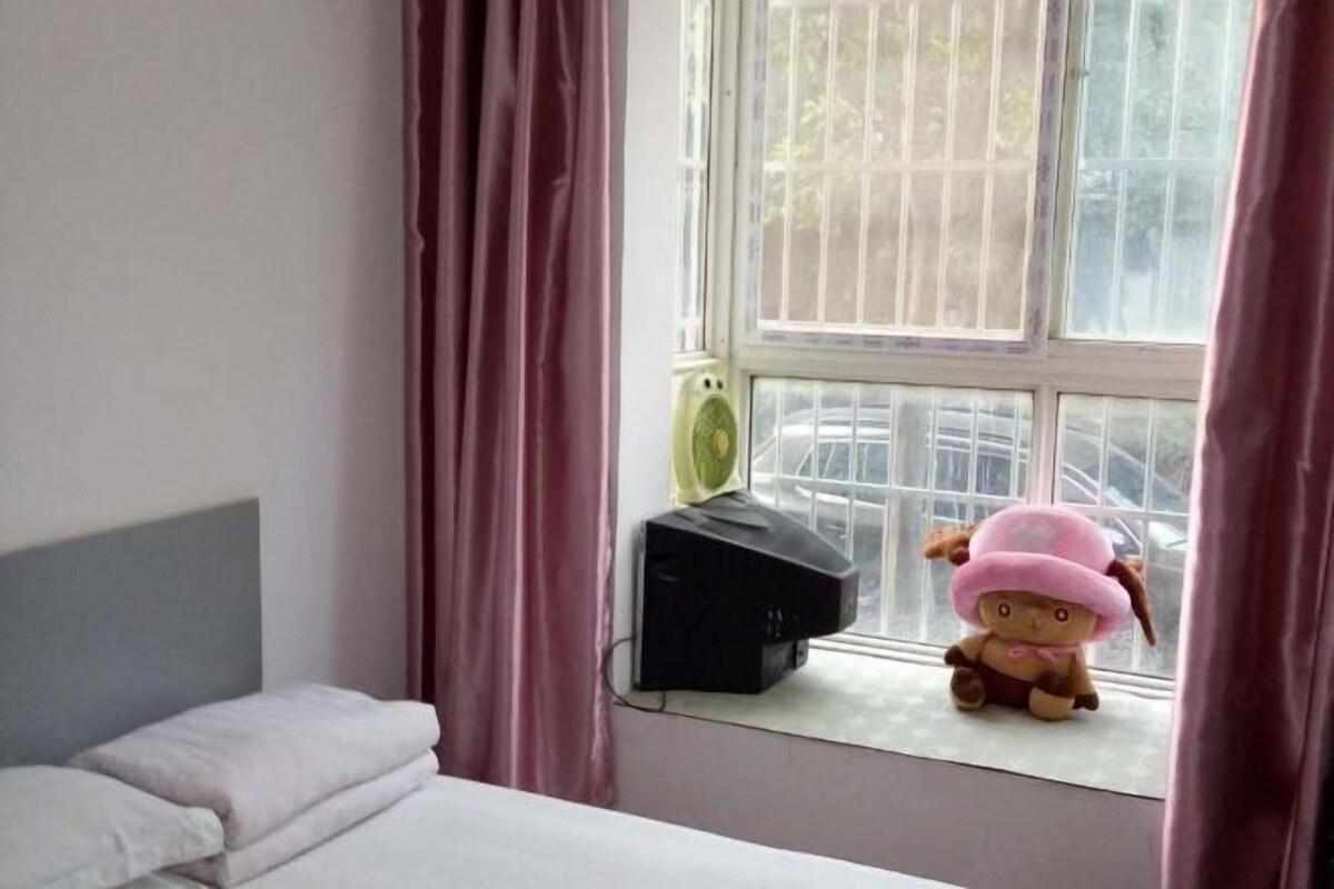 A bedroom with a bed, a window with curtains, a radiator, and a stuffed toy on the windowsill.