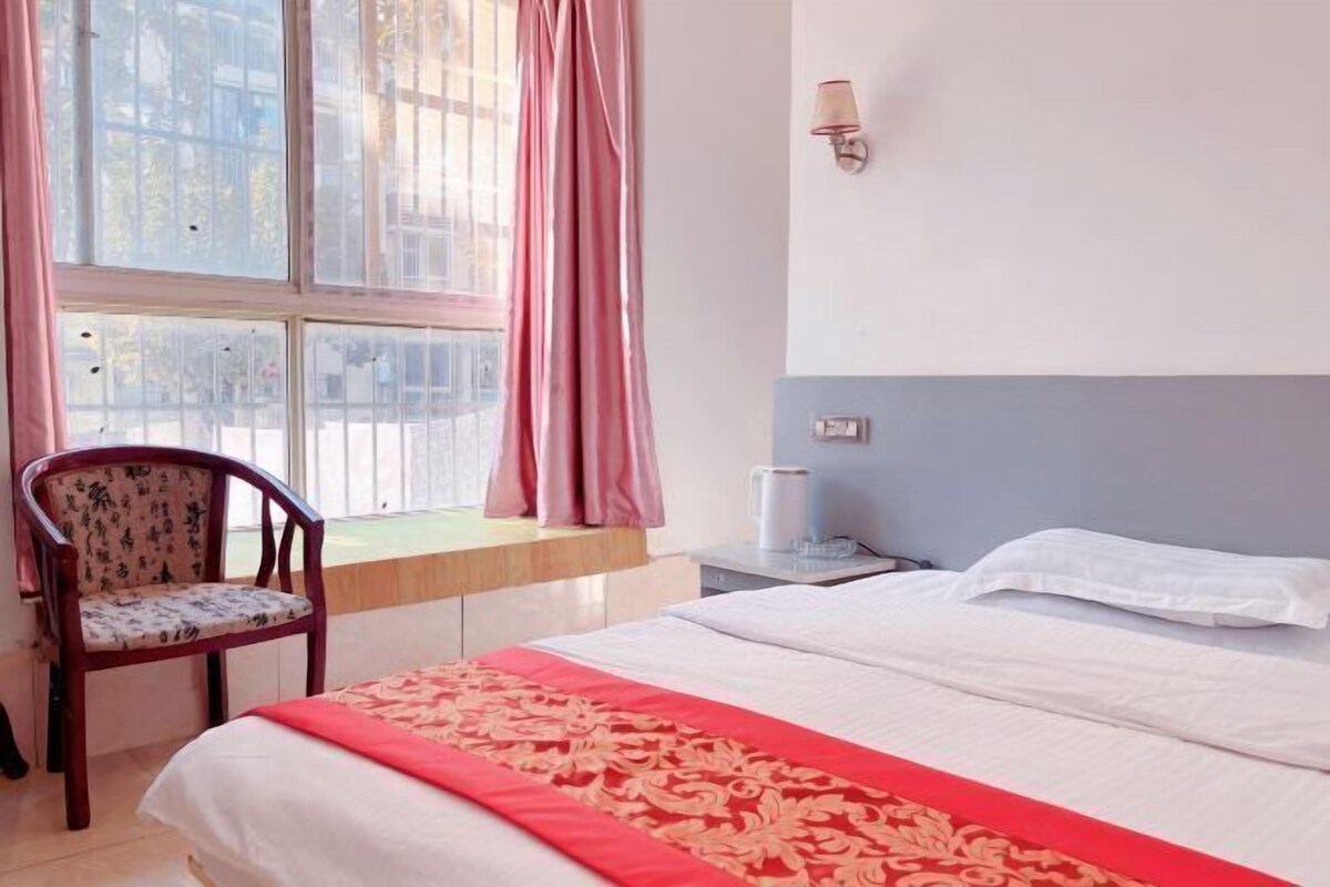 A hotel room with a bed, a chair, a nightstand, and a window with curtains.