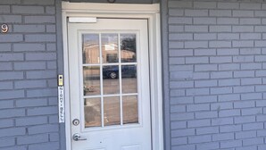 A building entrance with a white door, a mailbox, and a trash can. - Packsaddle Motel (Kingsland)
