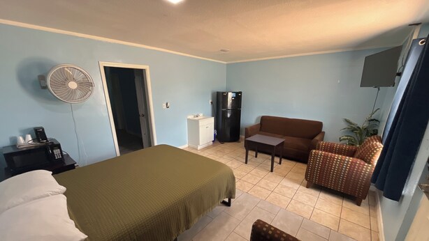 A hotel room with a bed, a sofa, a small table, a fan, a refrigerator, and a TV. - Packsaddle Motel (Kingsland)