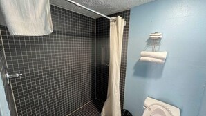 A bathroom with a shower, toilet, and towel rack. - Packsaddle Motel (Kingsland)