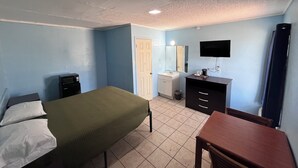 A bedroom with a bed, a desk, a dresser, a mirror, and a television. - Packsaddle Motel (Kingsland)