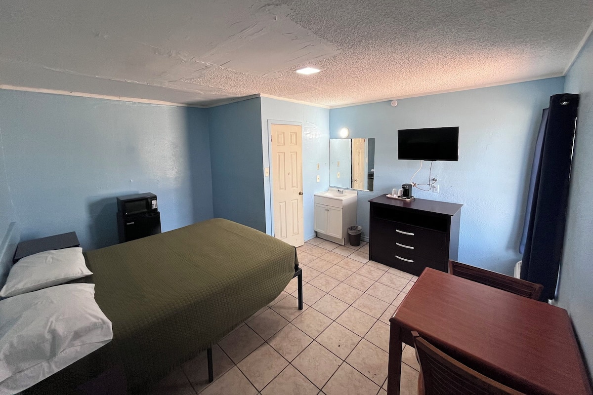 A bedroom with a bed, a desk, a dresser, a mirror, and a television.