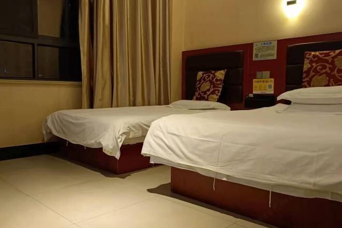 A hotel room with two beds, a window with curtains, and a wall with a sign.