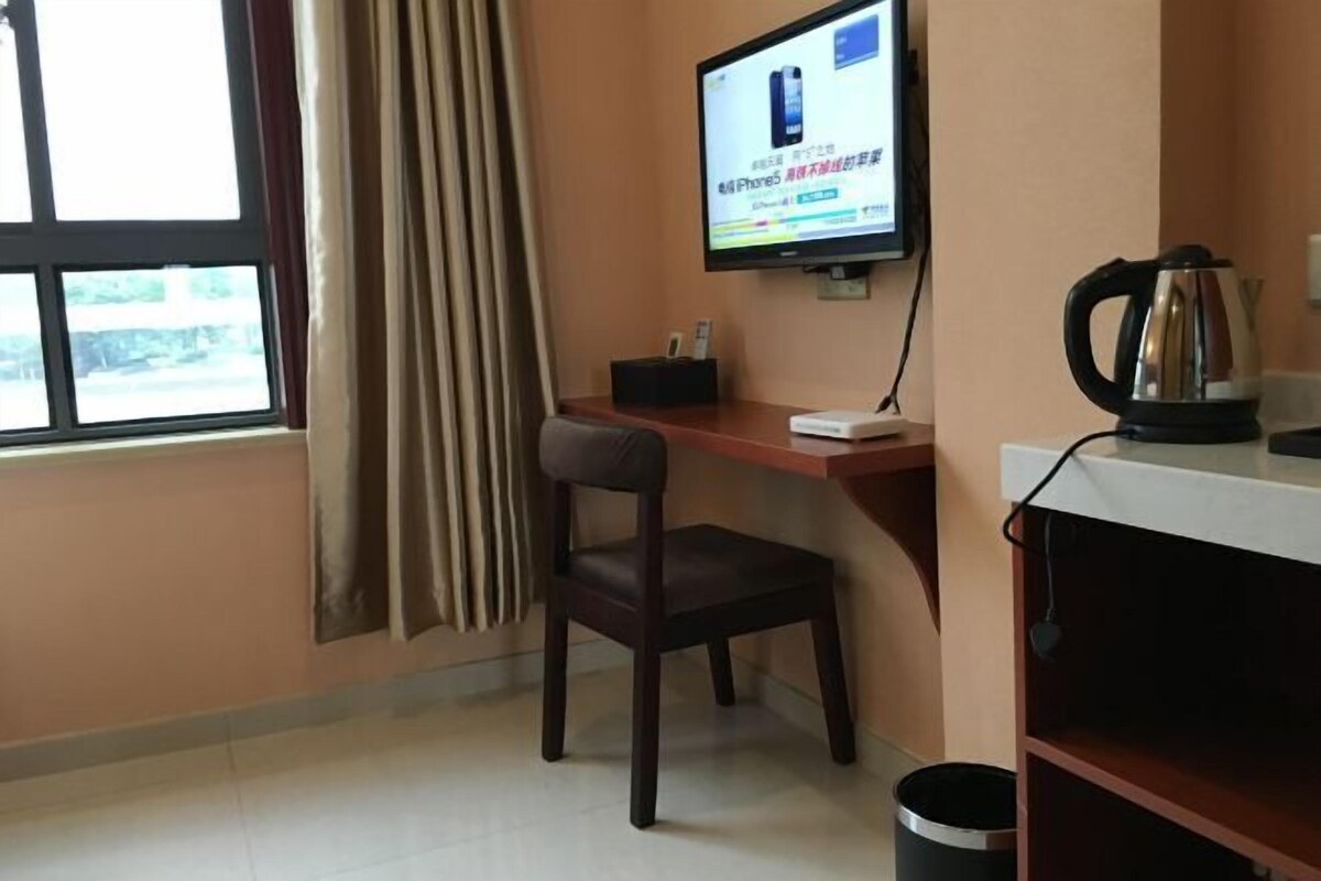 A hotel room with a desk, chair, television, kettle, and a window with curtains.