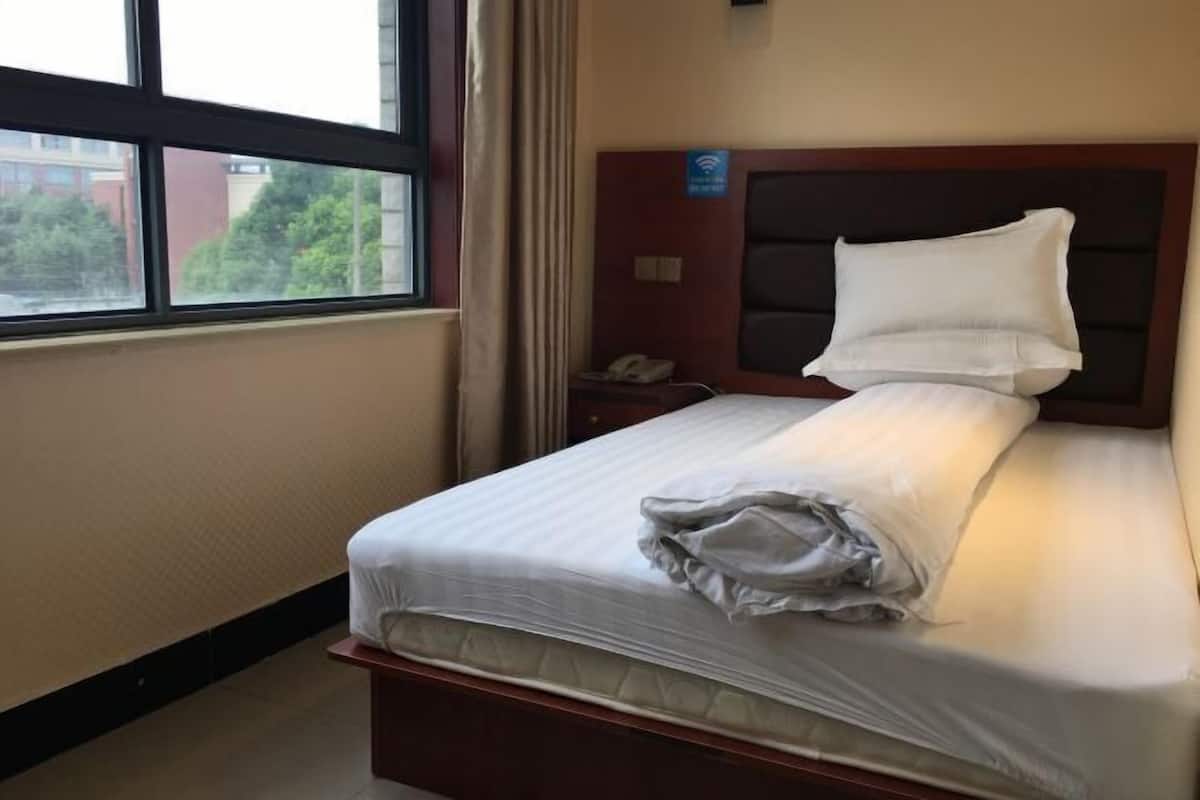 A hotel room with a bed, a nightstand, a telephone, and a window with a view of buildings and trees.