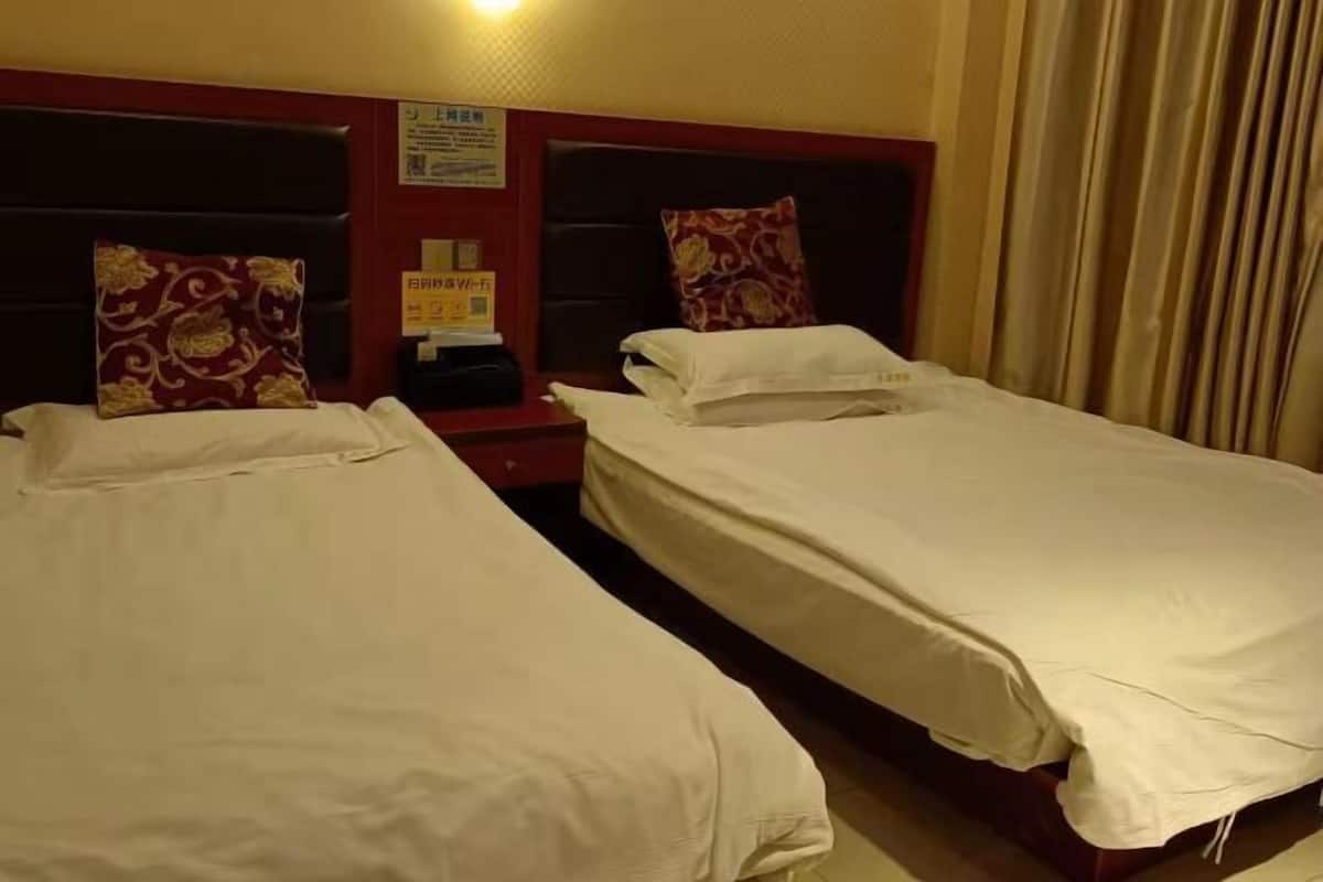 A hotel room with two single beds, a nightstand, and a wall-mounted clock.