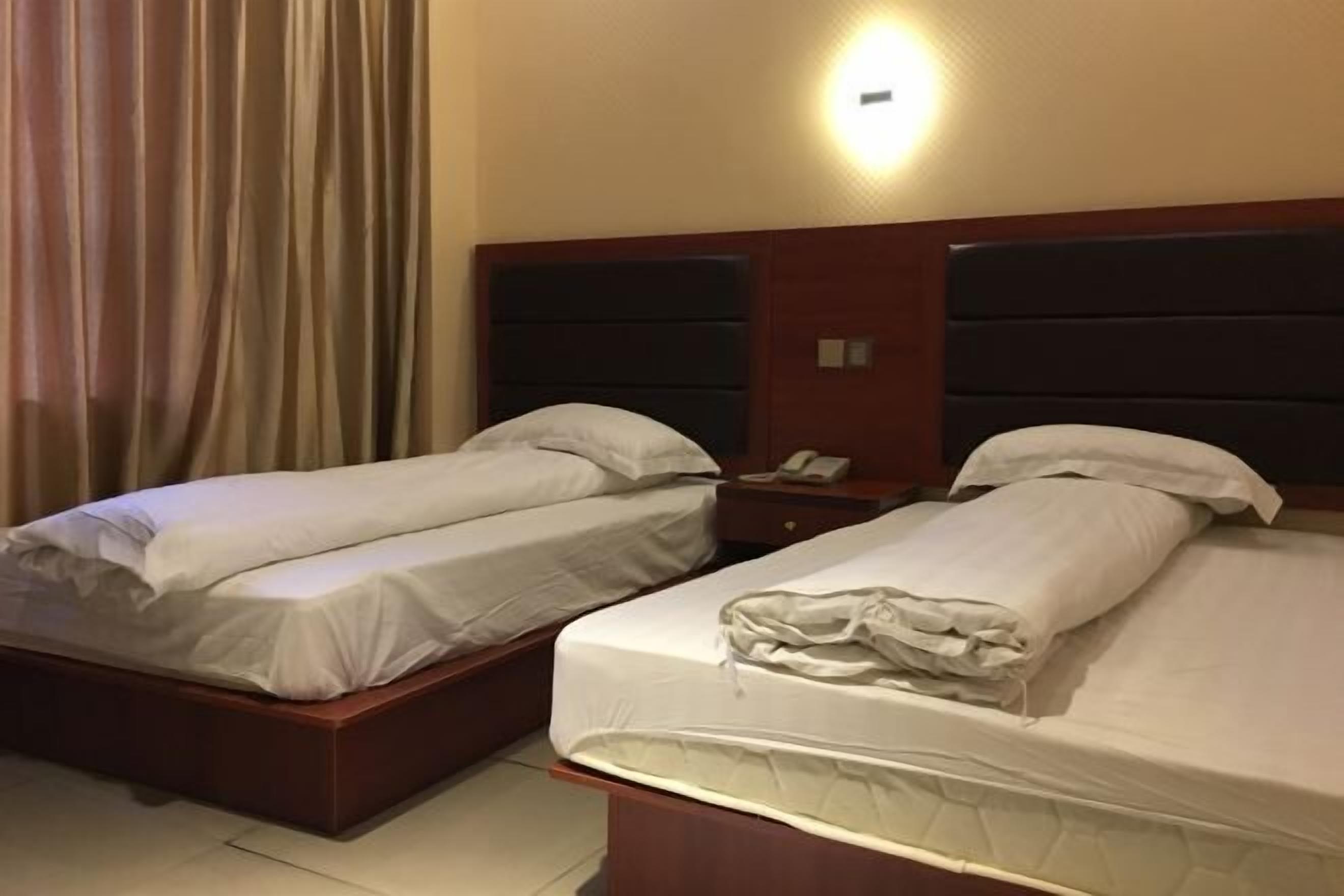 A hotel room with two single beds, a nightstand with a phone, and a wall-mounted light.