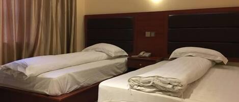 A hotel room with two single beds, a nightstand with a phone, and a wall-mounted light.