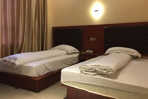 A hotel room with two single beds, a nightstand with a phone, and a wall-mounted light. - Xinglan Hotel (Shanghai)