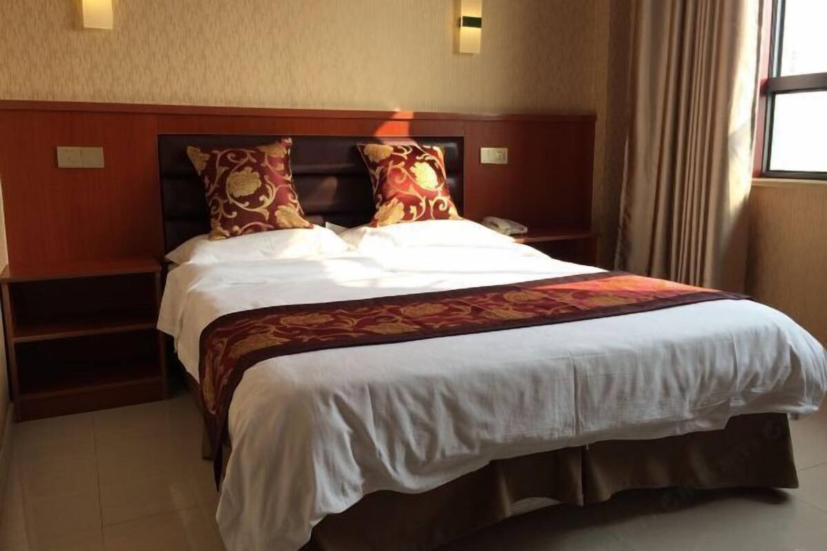 A hotel room with a large bed, two bedside tables, a nightstand, and a window with curtains.