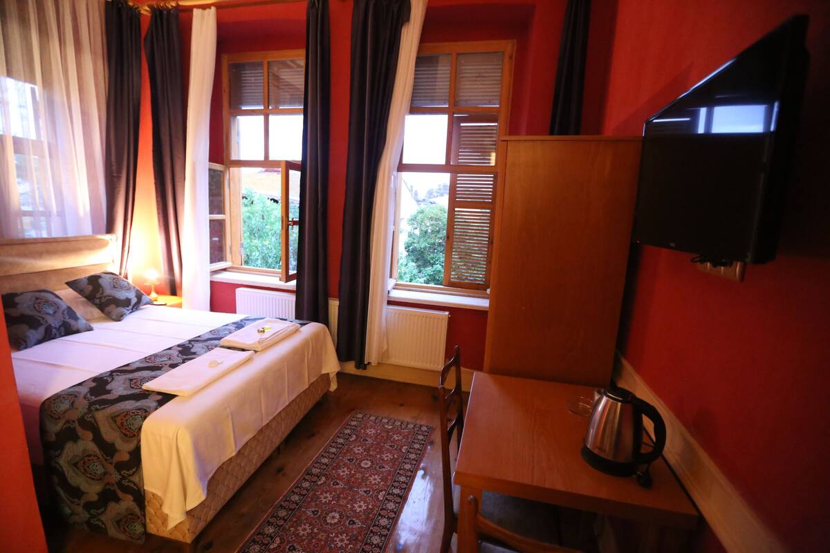 A hotel room with a bed, a desk, a chair, a television, and a window with curtains.