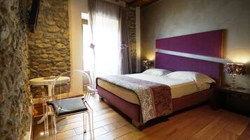 Ein Schlafzimmer mit Steinwand, einem Bett mit violettem Kopfteil, einem Nachttisch mit Lampe und einem kleinen runden Tisch mit Stuhl.