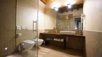 A modern bathroom with a glass shower enclosure, a white toilet, a bidet, a sink, and a vanity with towels.