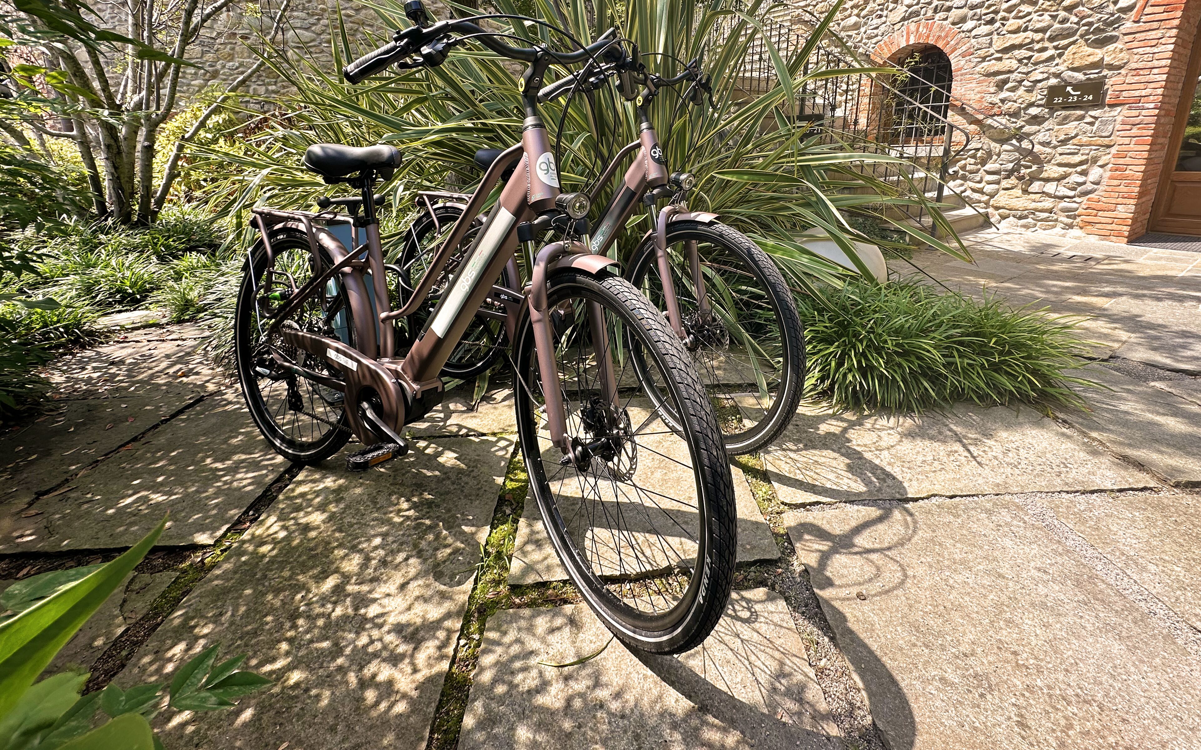 Una bicicleta estática aparcada sobre un sendero de piedra, con un muro de piedra y vegetación al fondo.