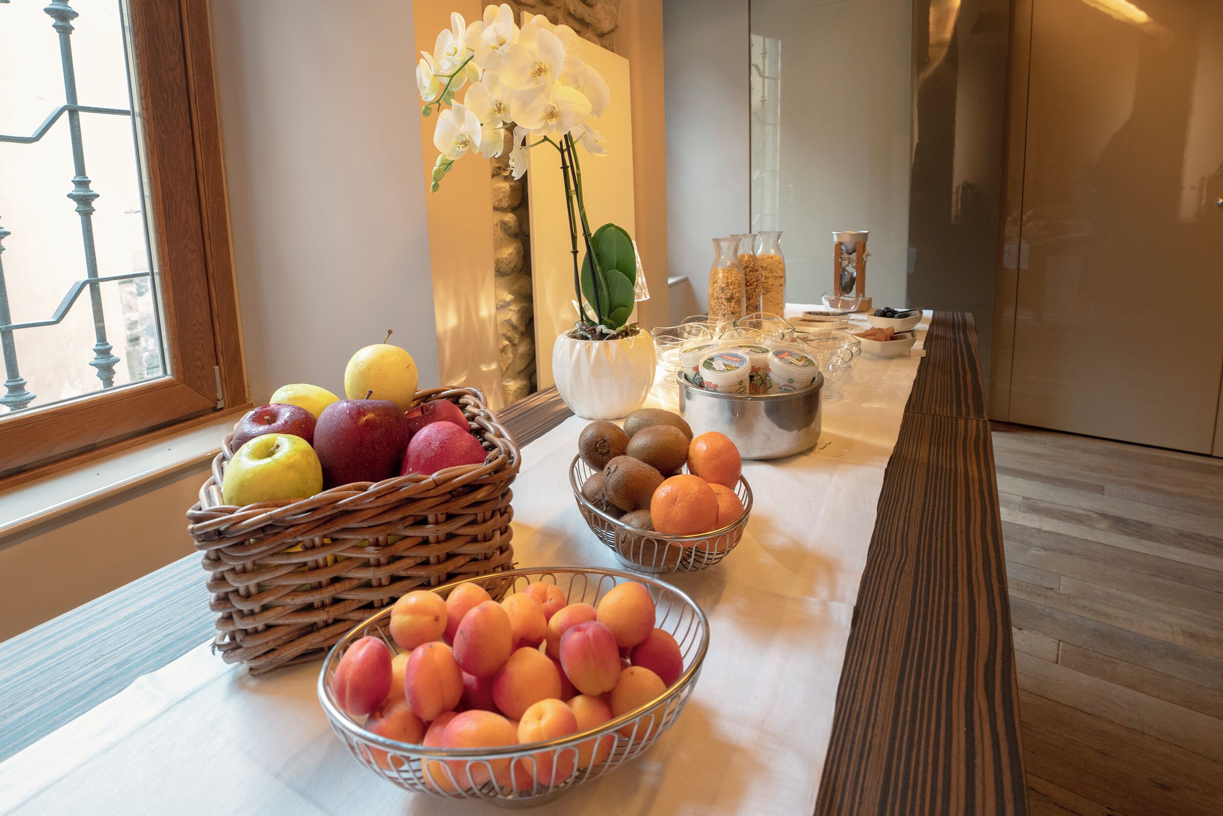 Un buffet de petit-déjeuner proposant une variété de fruits et agrémenté d’un vase rempli d’orchidées blanches.