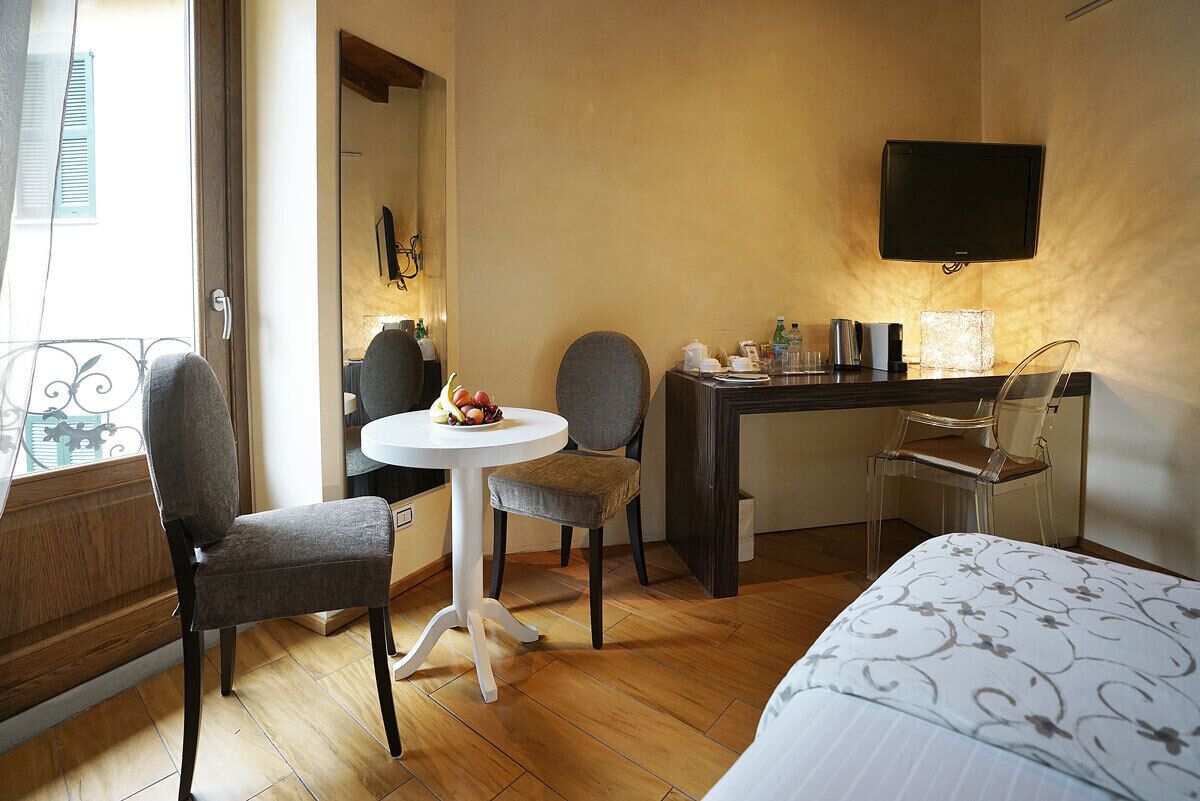 Une chambre d’hôtel avec un lit, un bureau et une chaise, une petite table ronde avec des fruits, un téléviseur fixé au mur et une fenêtre avec des stores.