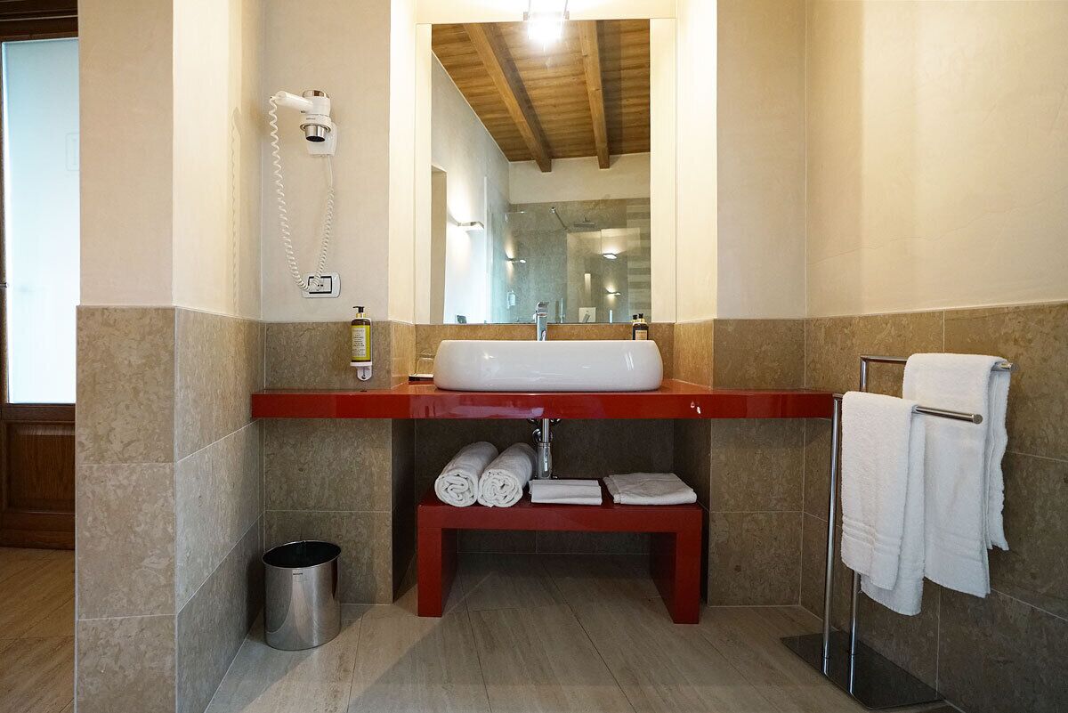 Ein Badezimmer mit einem weißen Waschbecken, einem Spiegel, einem Handtuchhalter und einer Sitzbank mit Handtüchern.