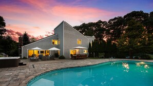 A two-story house with a swimming pool, outdoor furniture, and a patio area.