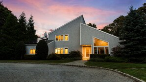 Et moderne hus i to etager med skråt tag, store vinduer og en velplejet græsplæne.