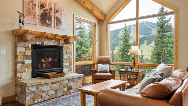 Ein gemütliches Wohnzimmer mit Kamin aus Stein, Ledersofa und großem Fenster mit Blick auf die Berge.