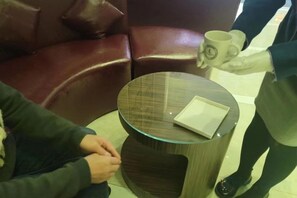 Een ronde glazen tafel met een boek en een kopje, een leren bank en een persoon die een kop vasthoudt.