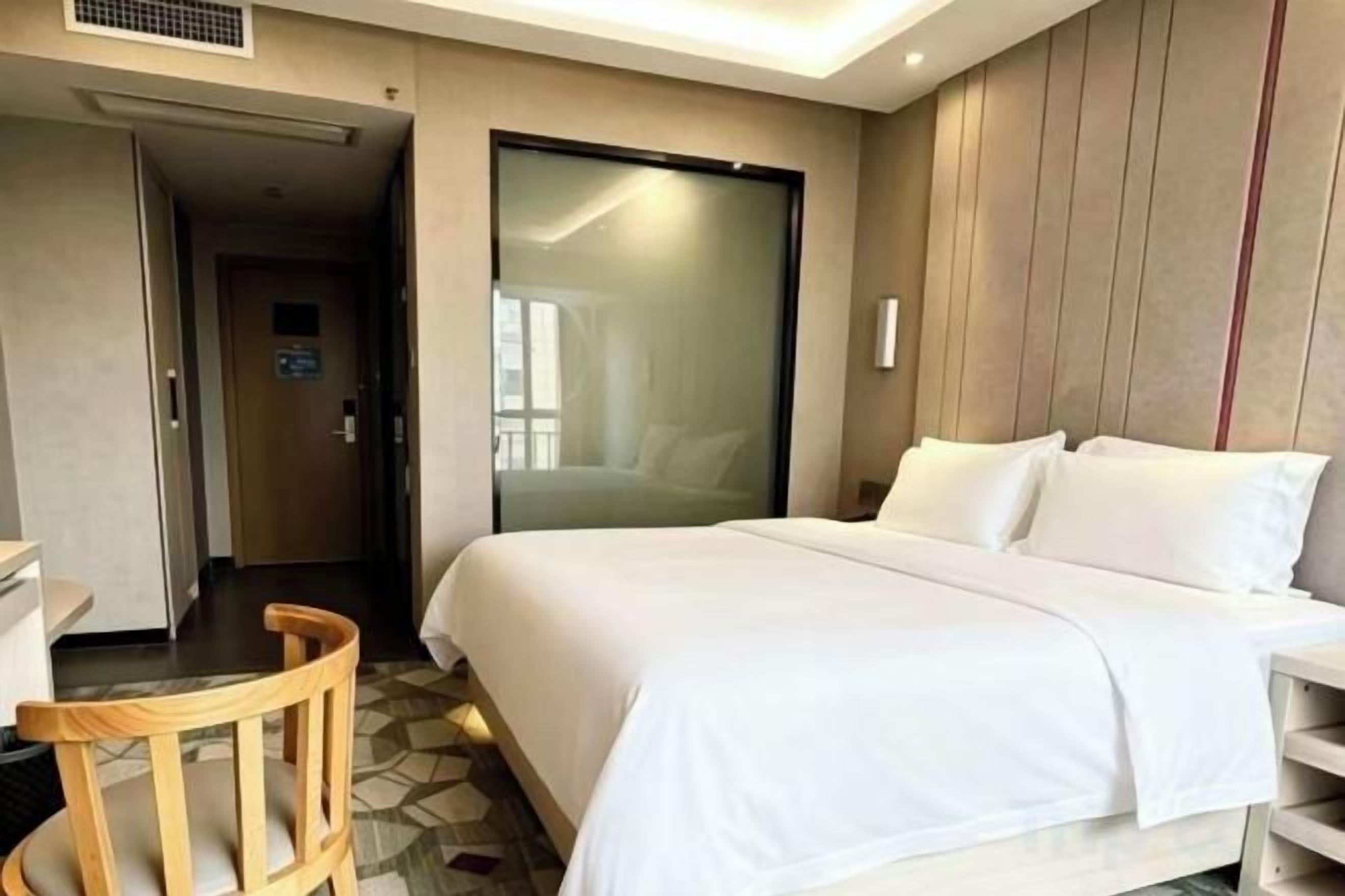 A hotel room with a bed, a chair, a desk, and a wardrobe.