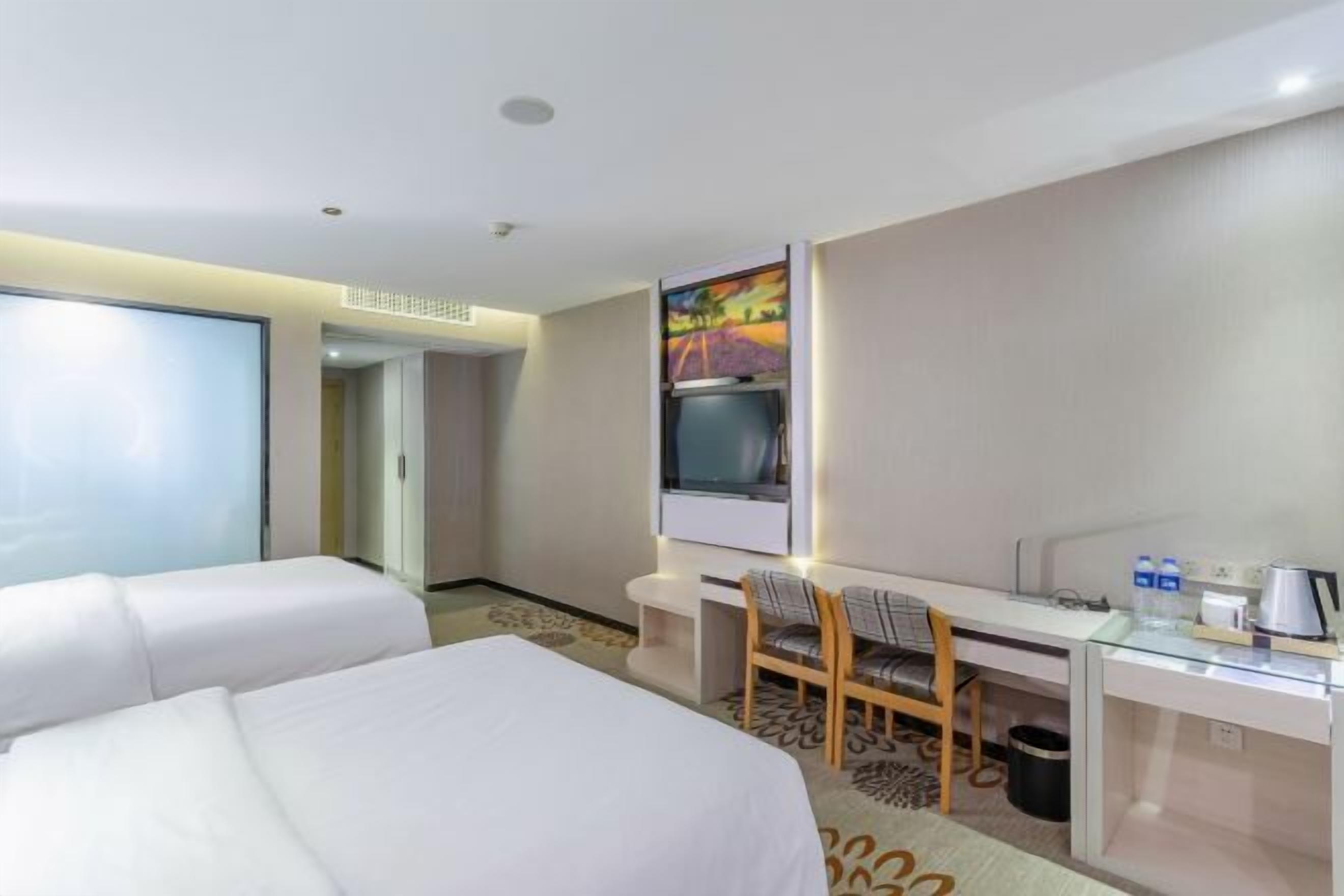 A hotel room with two beds, a desk with a chair, a TV, and a window.