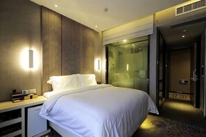 A modern hotel room with a large bed, bedside table, and a glass shower area.