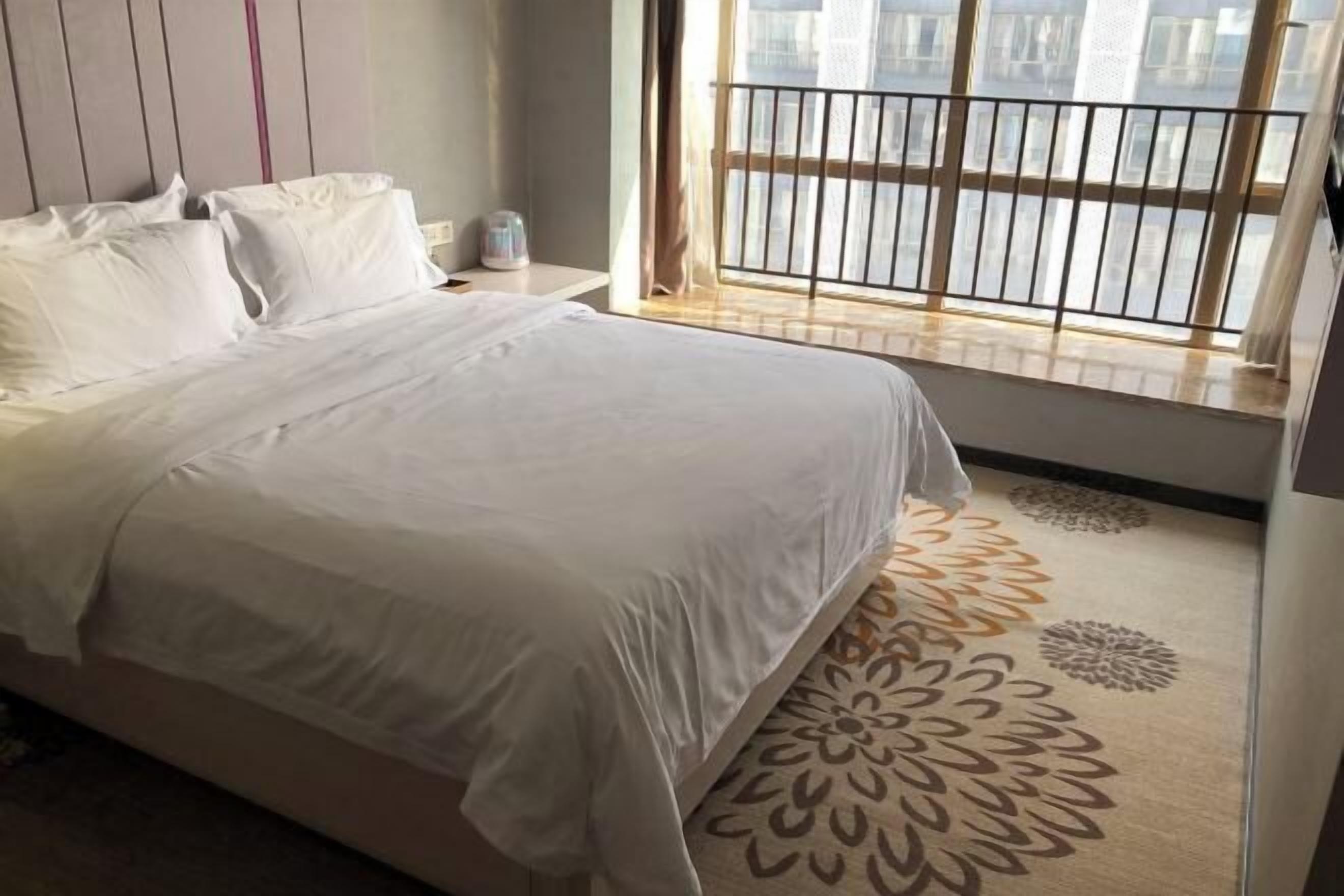 A neatly made bed with white linens in a hotel room with a large window offering a view of the city.
