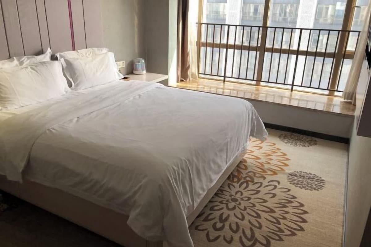 Un letto rifatto con lenzuola bianche in una camera d'albergo con un'ampia finestra che offre vista sulla città.