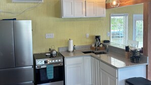 A kitchen with a stove, oven, and refrigerator, wooden beams, a window, and a sink. - Hellgate Island scallop house, boat access only (Homosassa)