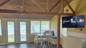A spacious living room with a wooden ceiling, a dining area with a table and chairs, a sofa, and a television mounted on the wall. - Hellgate Island scallop house, boat access only (Homosassa)