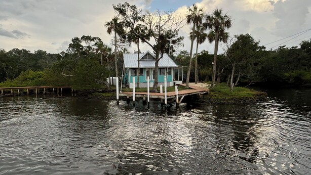 A houseboat with a small deck and a covered porch, surrounded by water and palm trees. - Hellgate Island scallop house, boat access only (Homosassa)