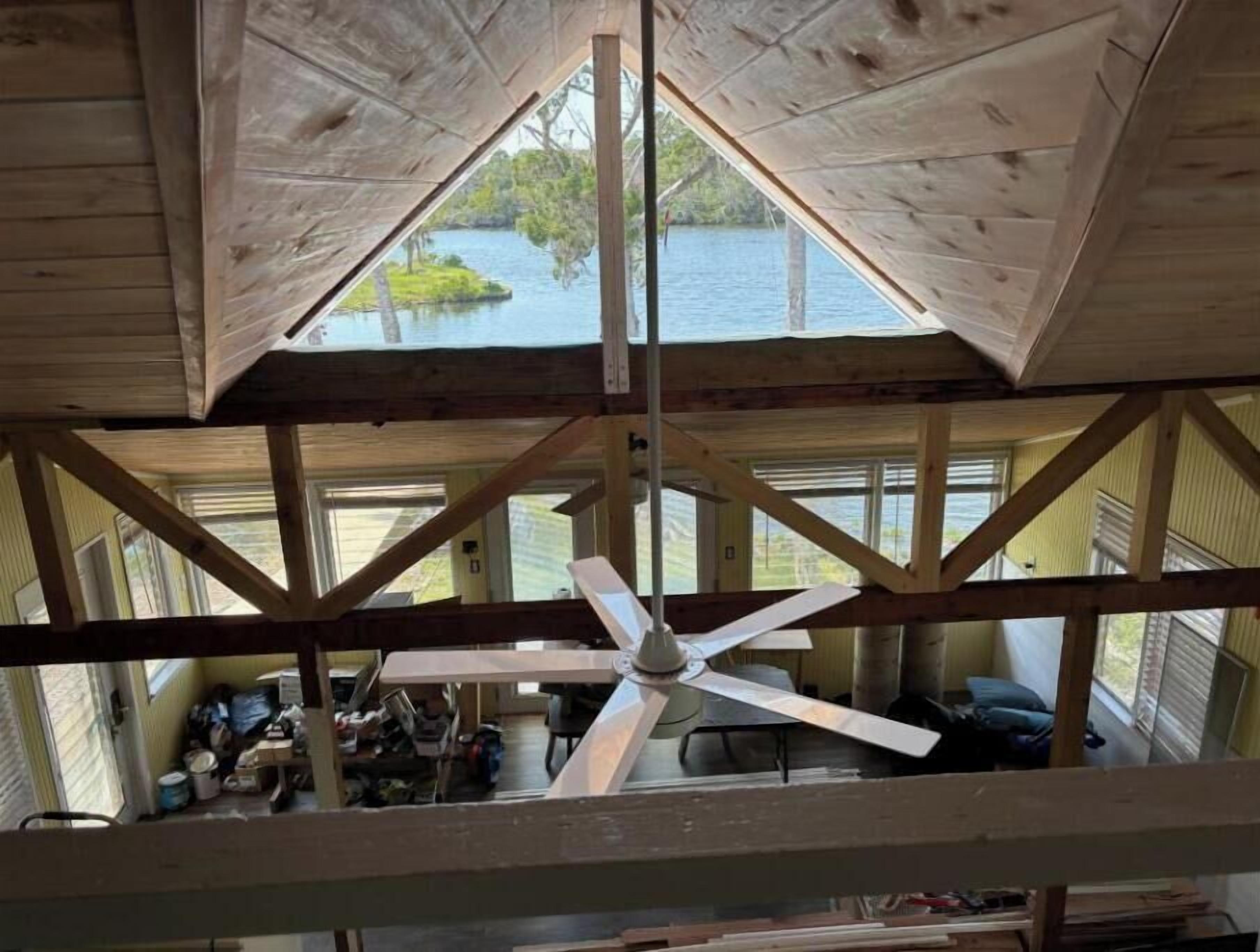 Eine hölzerne Konstruktion mit hohen Decken, einem zentralen Ventilator, großen Fenstern und Blick auf ein Gewässer.