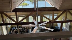 A high-ceilinged wooden structure with a central fan, large windows, and a view of a body of water. - Hellgate Island scallop house, boat access only (Homosassa)