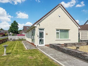Ein eingeschossiges Haus mit weißer Fassade, einer grünen Tür und einem kleinen Vorgarten.