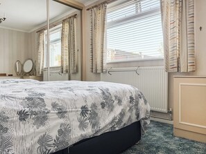 Ein Schlafzimmer mit einem Bett, einem Spiegel, Vorhängen und einer Heizung.