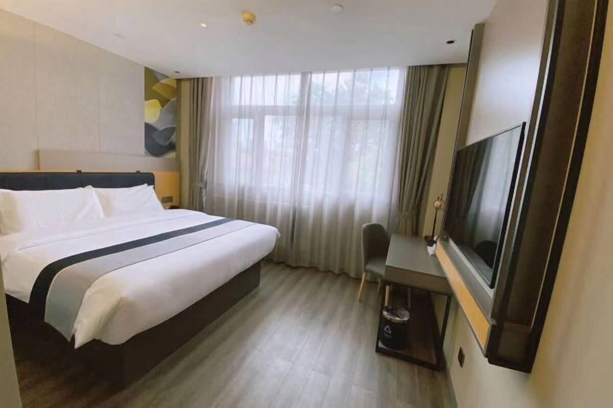 A hotel room with a bed, a desk with a chair, a television, and a window with curtains.