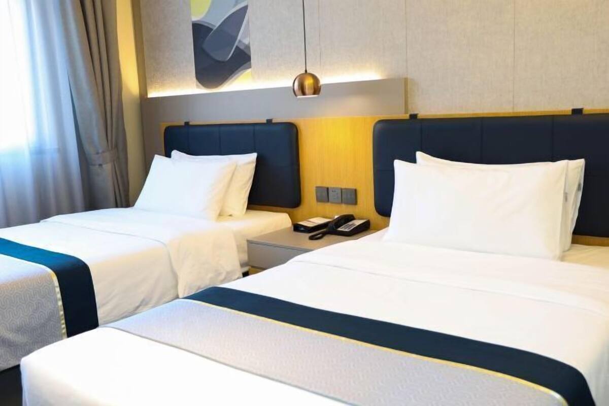 A hotel room with two beds, a bedside table with a phone, and a wall-mounted light fixture.